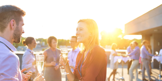 Two people smiling at a party joined by other people behind them