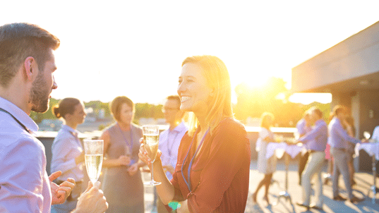 Two people smiling at a party joined by other people behind them
