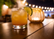 Cocktail with a lime next to a candle on a table at night