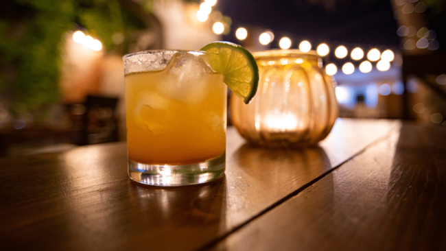 Cocktail with a lime next to a candle on a table at night