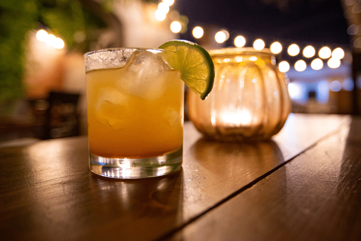 Cocktail with a lime next to a candle on a table at night